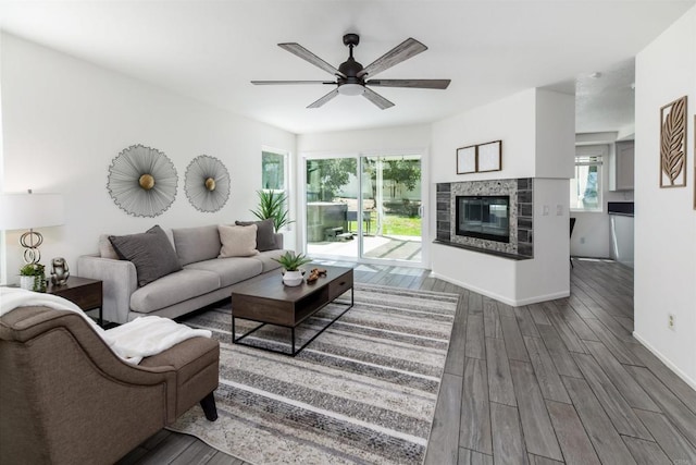 living room with baseboards, ceiling fan, a glass covered fireplace, and wood finished floors