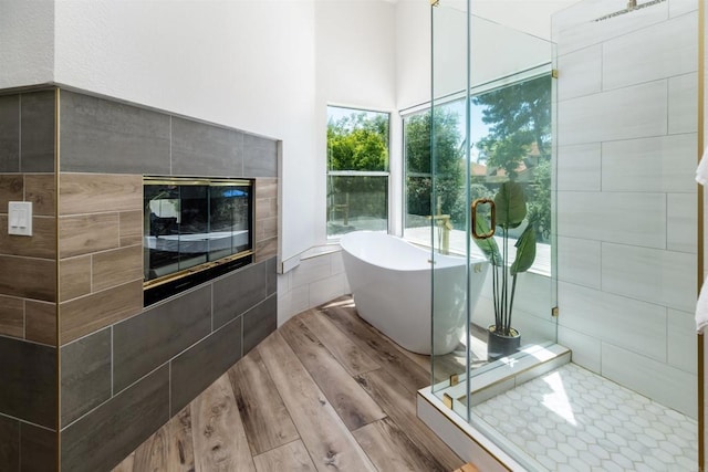 full bathroom featuring a soaking tub, a stall shower, wood finished floors, and a tile fireplace