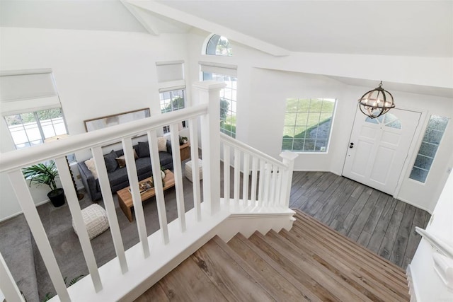 stairs featuring an inviting chandelier, plenty of natural light, vaulted ceiling with beams, and wood finished floors