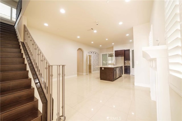 stairs with arched walkways, tile patterned flooring, baseboards, and recessed lighting