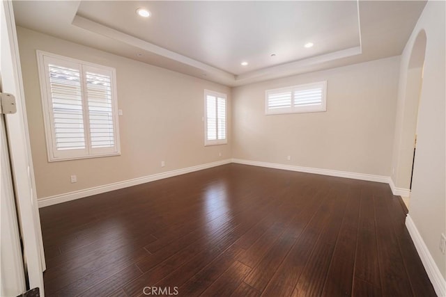 unfurnished room with baseboards, a tray ceiling, dark wood finished floors, and arched walkways