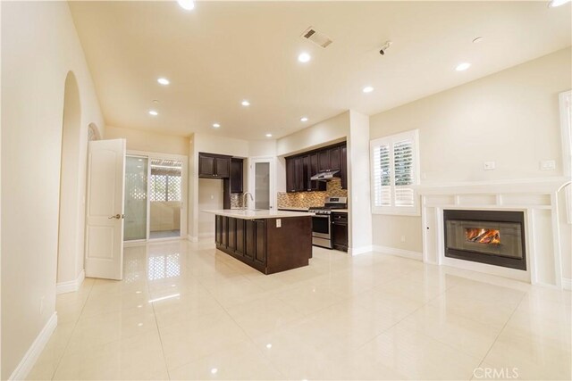 kitchen featuring open floor plan, stainless steel range with gas cooktop, light countertops, under cabinet range hood, and backsplash