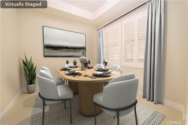 tiled dining space featuring baseboards and a raised ceiling