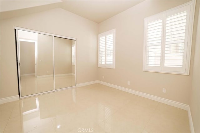 unfurnished bedroom featuring vaulted ceiling, baseboards, tile patterned flooring, and a closet