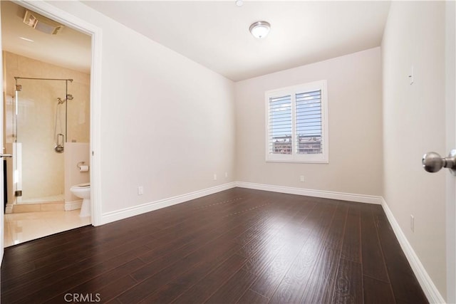 empty room with dark wood-style flooring, baseboards, and visible vents