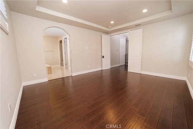 spare room featuring arched walkways, recessed lighting, dark wood-style floors, and a raised ceiling