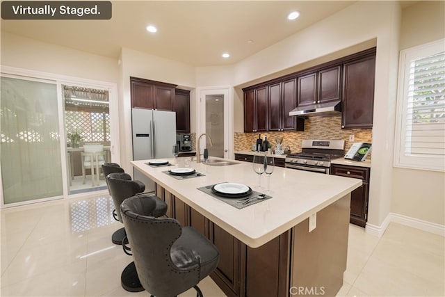 kitchen with decorative backsplash, a sink, stainless steel gas range, freestanding refrigerator, and under cabinet range hood