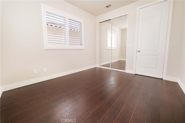 unfurnished bedroom with dark wood-type flooring, baseboards, visible vents, and a closet