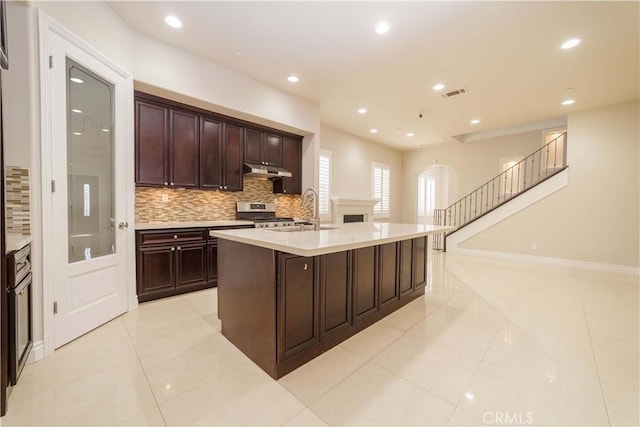 kitchen with a sink, stainless steel gas range oven, backsplash, under cabinet range hood, and visible vents