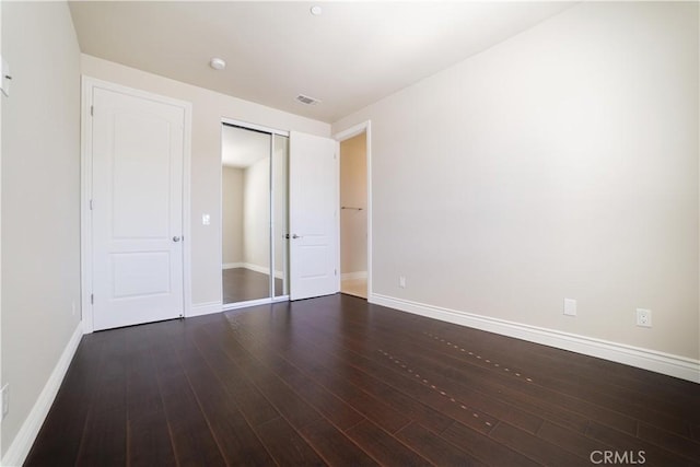 unfurnished bedroom featuring baseboards, a closet, wood finished floors, and visible vents