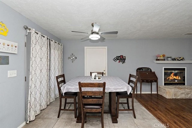 dining space with a textured ceiling, baseboards, ceiling fan, and light tile patterned floors
