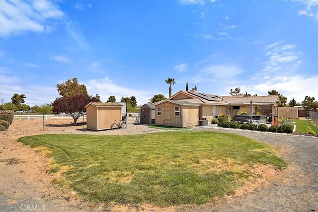 view of front of home with a storage shed, a front lawn, roof mounted solar panels, fence, and an outbuilding