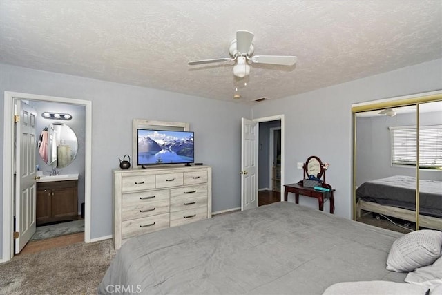 carpeted bedroom with a textured ceiling, ensuite bathroom, a sink, a closet, and visible vents