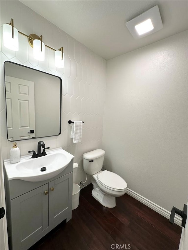half bath with vanity, baseboards, toilet, and wood finished floors