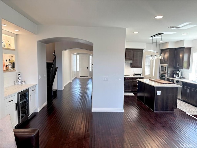 kitchen featuring appliances with stainless steel finishes, dark wood-style flooring, arched walkways, and beverage cooler
