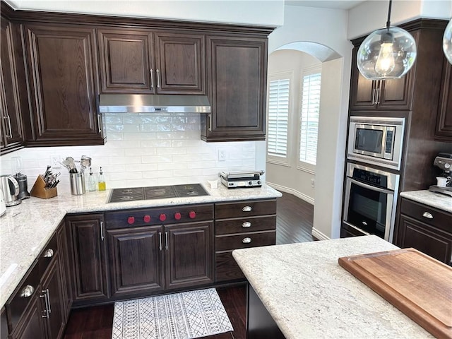 kitchen with under cabinet range hood, tasteful backsplash, dark brown cabinets, and stainless steel appliances