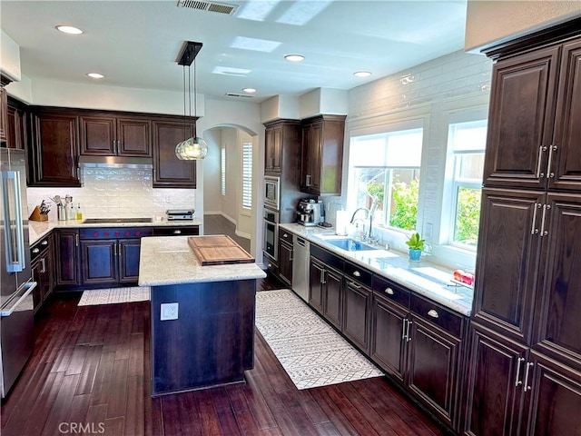 kitchen featuring a sink, arched walkways, stainless steel appliances, dark wood-type flooring, and a kitchen island