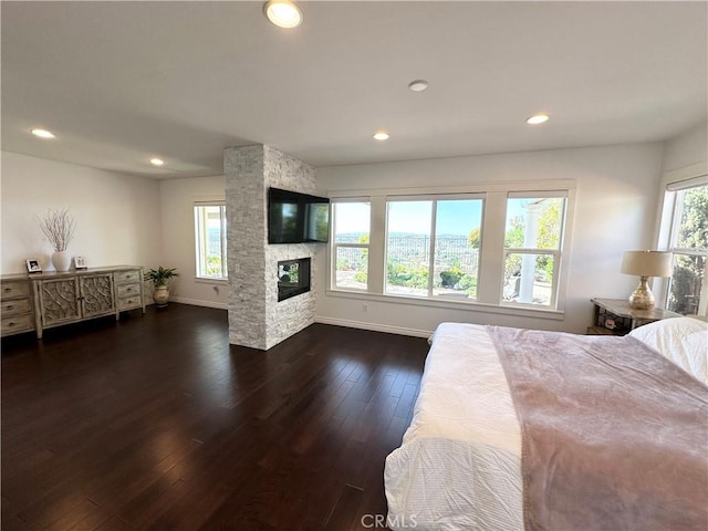 bedroom with baseboards, recessed lighting, dark wood-style flooring, and a stone fireplace