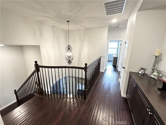 hallway featuring baseboards, visible vents, dark wood-type flooring, and an upstairs landing