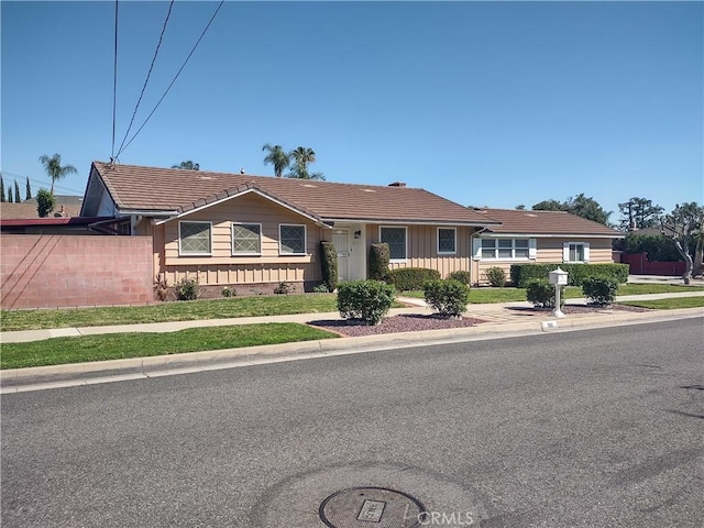 view of front of property with board and batten siding, a tiled roof, and fence