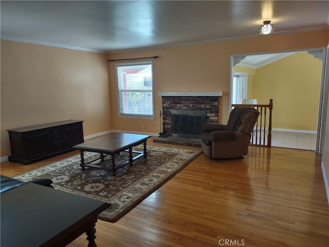 living area with baseboards, crown molding, a brick fireplace, and wood finished floors