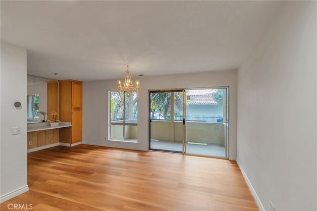 unfurnished dining area featuring light wood-type flooring, a notable chandelier, and baseboards