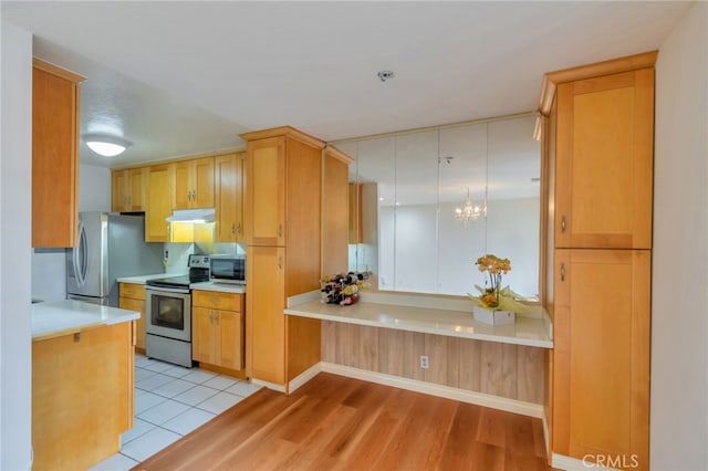 kitchen featuring a chandelier, under cabinet range hood, light wood-style floors, light countertops, and appliances with stainless steel finishes