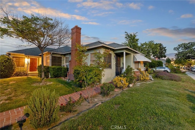 property exterior at dusk with a lawn, a chimney, and stucco siding