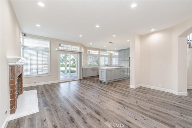 429 Somerset Cir, Corona, CA 92879 - unfurnished living room featuring baseboards, arched walkways, recessed lighting, light wood-type flooring, and a brick fireplace