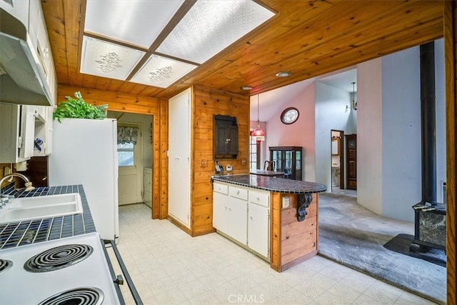 kitchen featuring lofted ceiling, white electric stove, a wood stove, a sink, and a peninsula