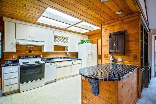 kitchen featuring a sink, tile countertops, wooden walls, white appliances, and under cabinet range hood