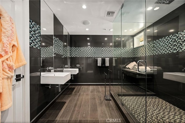 full bath featuring a sink, wood finished floors, a stall shower, double vanity, and visible vents