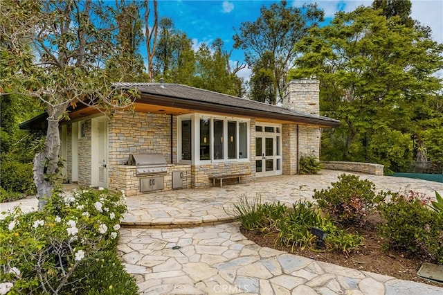 rear view of house featuring a chimney, exterior kitchen, a patio area, french doors, and stone siding