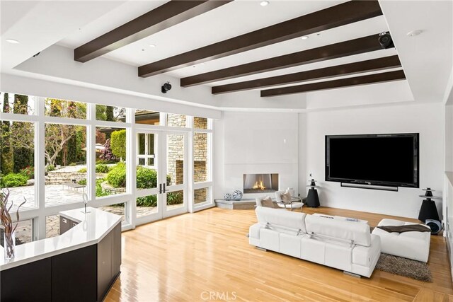 living area featuring light wood-type flooring, beam ceiling, a wealth of natural light, and french doors