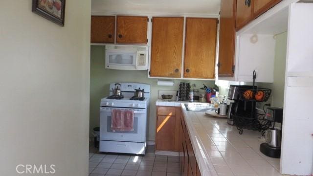 506 N Sunset Ave, Azusa, CA 91702 - kitchen with tile countertops, white appliances, tile patterned floors, brown cabinetry, and a wood stove