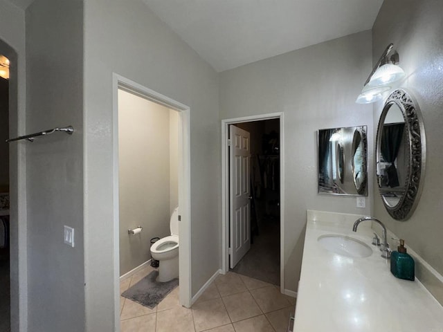 full bath with tile patterned floors, toilet, vanity, a walk in closet, and baseboards