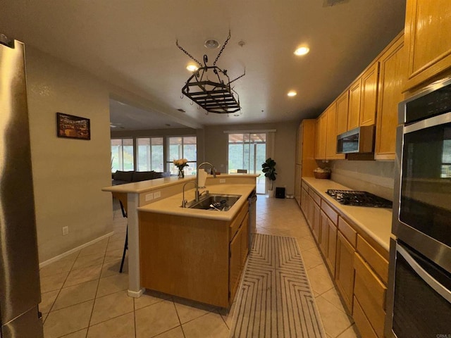 kitchen with a kitchen island with sink, appliances with stainless steel finishes, light tile patterned floors, and a sink