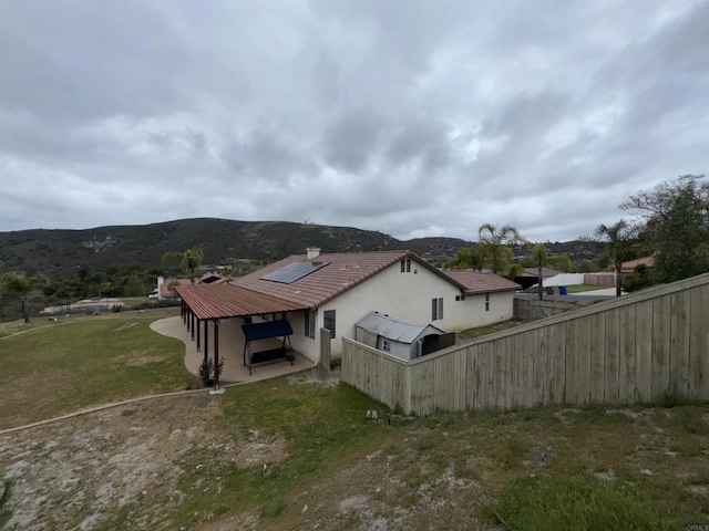 view of side of home featuring roof mounted solar panels, a chimney, fence, stucco siding, and a mountain view