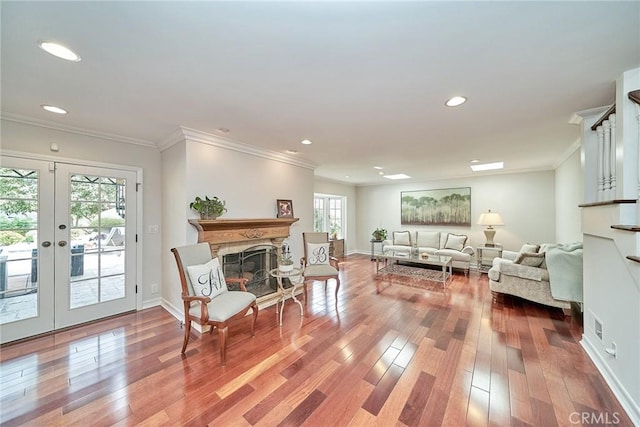 living area with crown molding, a fireplace with raised hearth, french doors, recessed lighting, and wood finished floors
