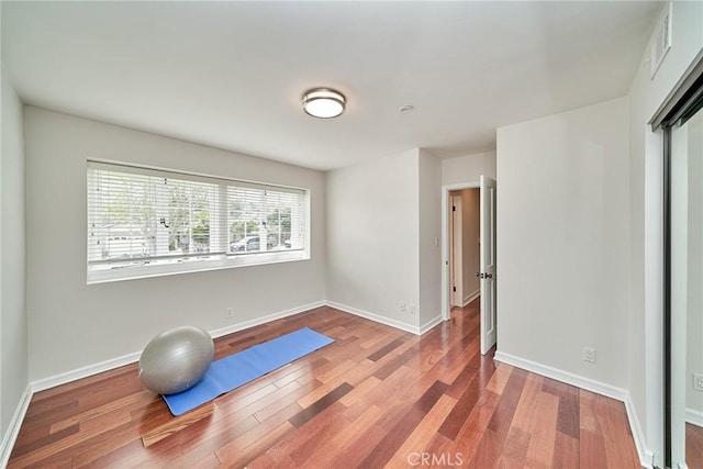 exercise room with baseboards, visible vents, and wood finished floors