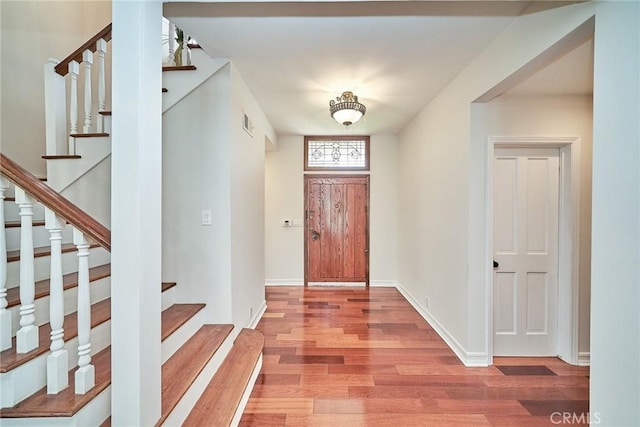 foyer entrance with baseboards, stairs, wood finished floors, and visible vents