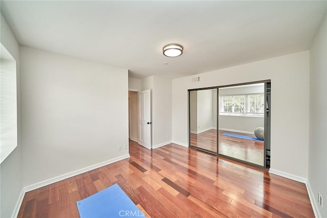 unfurnished bedroom featuring visible vents, baseboards, wood finished floors, and a closet