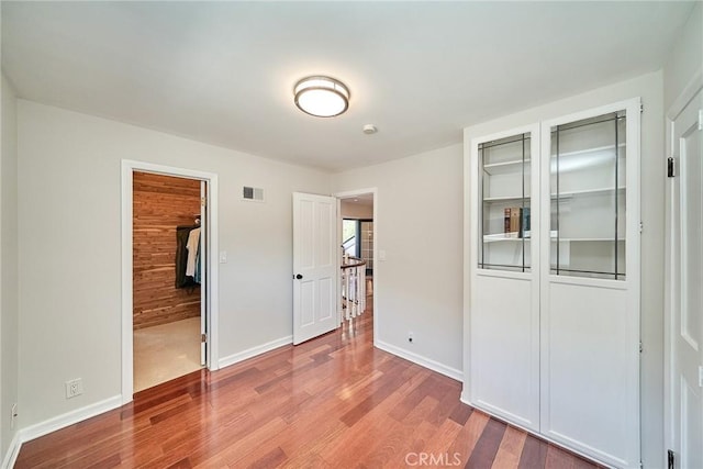 unfurnished bedroom featuring baseboards, a closet, wood finished floors, and visible vents