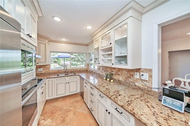 kitchen with a sink, built in appliances, crown molding, and backsplash