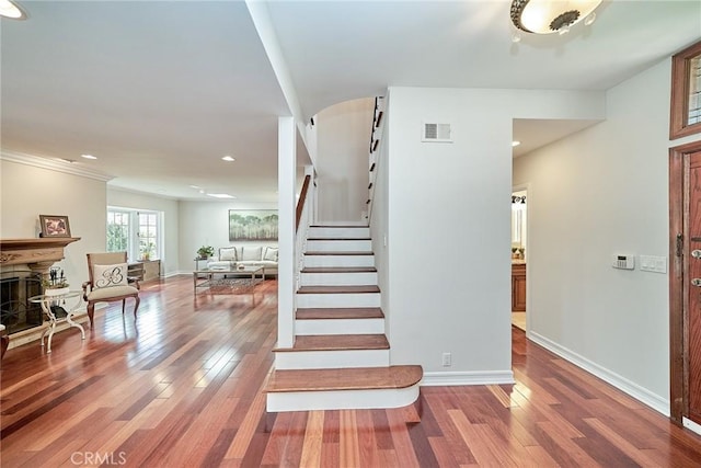 staircase featuring baseboards, a fireplace with raised hearth, wood finished floors, and visible vents
