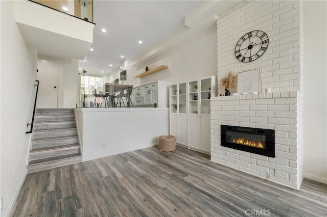 unfurnished living room with baseboards, a brick fireplace, wood finished floors, and stairs