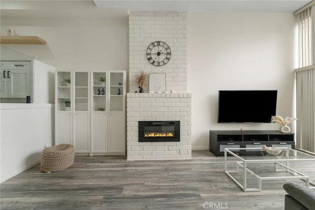 living area featuring baseboards, a brick fireplace, and wood finished floors