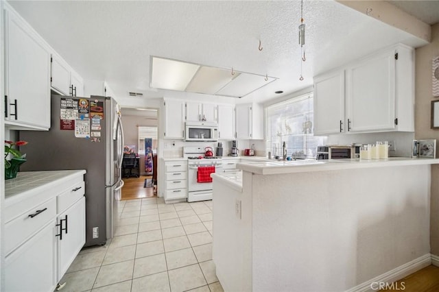 kitchen with white cabinets, a peninsula, white appliances, and light tile patterned flooring