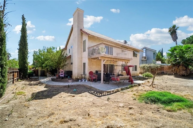 back of property featuring a balcony, a chimney, a fenced backyard, a patio, and stucco siding