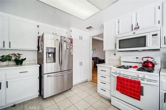 kitchen featuring white cabinets, visible vents, light tile patterned flooring, and white appliances